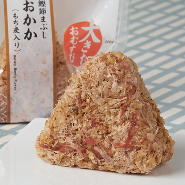 ファミリーマートの【九州】もち麦 大きなおむすび おかか（鰹節まぶし）を比較する。税込価格：235円。もち麦入りのだしご飯に甘めのおかかを混ぜ込みました。表面にかつお節をまぶした仕立てです。
