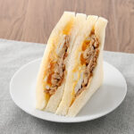 ファミリーマートのテリヤキチキンとたまごのサンドを比較する。税込価格：348円。甘辛く味付けしたテリヤキチキンを、コクのあるタマゴサラダとゆでたまごと合わせました。