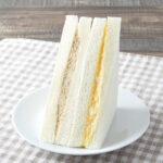ファミリーマートのツナとたまごサンド。税込価格：298円、カロリー：307kcal、たんぱく質：9.1g、脂質：18.2g、炭水化物：27.4g、食塩相当量：1.2g。みじん切りした玉ねぎを加えたツナサラダと、たまごのコクを感じるたまごサンドの2種類の味が楽しめる仕立てです。アレルギー：小麦、卵、乳成分、大豆、豚肉、りんご。