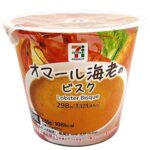 セブンイレブンの７プレミアム オマール海老のビスクを比較する。税込価格：322円、カロリー：108kcal、1円あたりカロリー：0.34kcal/円、たんぱく質：4.1g、1円あたりたんぱく質：0.01g/円、脂質：4.4g、炭水化物：14.3g、糖質：11.8g、食物繊維：2.5g、食塩相当量：1.6g。濃厚な甲殻類の風味に香味野菜とトマトを加えた旨味たっぷりのスープです。アレルギー：乳、えび。