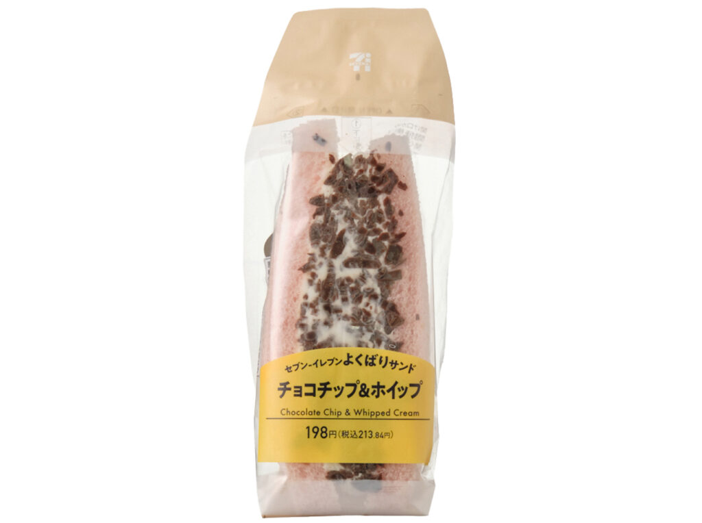 セブンイレブンのよくばりサンド チョコチップ＆ホイップ。税込価格：214円、カロリー：265kcal、たんぱく質：3.5g、脂質：17.6g、炭水化物：23.5g、糖質：22.7g、食物繊維：0.8g、食塩相当量：0.3g。手軽に手に取れる１組のホイップサンドです。表面には削りチョコ、中にはチョコチップが入っていて食感が良い仕立てです。アレルギー：卵、乳、小麦。