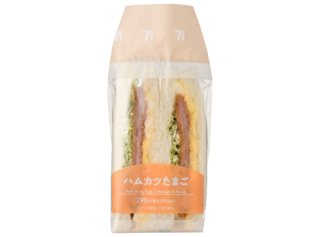 セブンイレブンのハムカツたまごサンドを比較する。税込価格：313円、カロリー：371kcal、1円あたりカロリー：1.18kcal/円、たんぱく質：10.2g、1円あたりたんぱく質：0.03g/円、脂質：19.7g、炭水化物：39.1g、糖質：37.2g、食物繊維：1.9g、食塩相当量：2.1g。たまごサラダと肉の旨味を感じるハムカツに濃厚なソースを組合わせました。アレルギー：卵、乳、小麦。