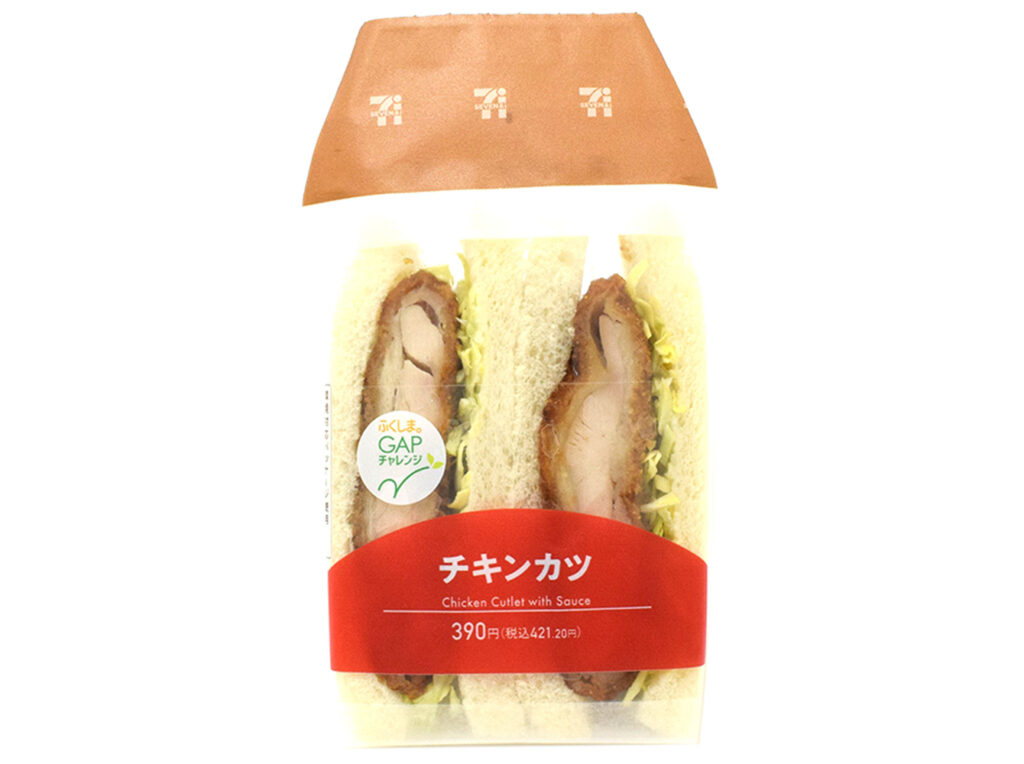セブンイレブンのチキンカツサンドを比較する。税込価格：421円、カロリー：413kcal、1円あたりカロリー：0.98kcal/円、たんぱく質：17.6g、1円あたりたんぱく質：0.04g/円、脂質：20.2g、炭水化物：41.1g、糖質：39.2g、食物繊維：1.9g、食塩相当量：2.4g。ソースを塗ったチキンカツとキャベツを盛り付けた食べ応えのあるサンドイッチです。アレルギー：卵、乳、小麦。