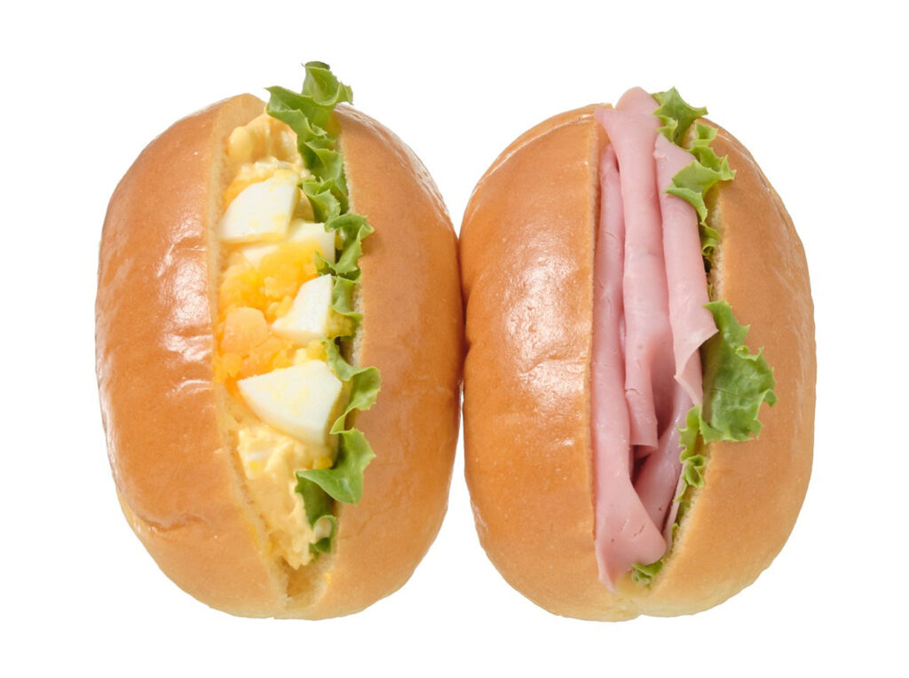 セブンイレブンのミニロールたまごサラダ＆ハムを比較する。税込価格：279円、カロリー：296kcal、たんぱく質：9g、脂質：15.6g、炭水化物：30.7g、糖質：29g、食物繊維：1.7g、食塩相当量：1.2g。定番具材のたまごとハムの２種類の味が楽しめる、手軽に持ち運びしやすいボックスタイプのロールです。アレルギー：卵、乳、小麦。