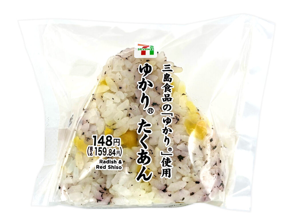 セブンイレブンのゆかりたくあんおむすびを比較する。税込価格：160円、カロリー：167kcal、1円あたりカロリー：1.04kcal/円、たんぱく質：2.7g、1円あたりたんぱく質：0.02g/円、脂質：0.7g、炭水化物：38.3g、糖質：36.6g、食物繊維：1.7g、食塩相当量：1.6g。出汁で炊いた御飯にゆかりとたくあんを混ぜ込んだ彩りと食感の良いおむすび。アレルギー：小麦。