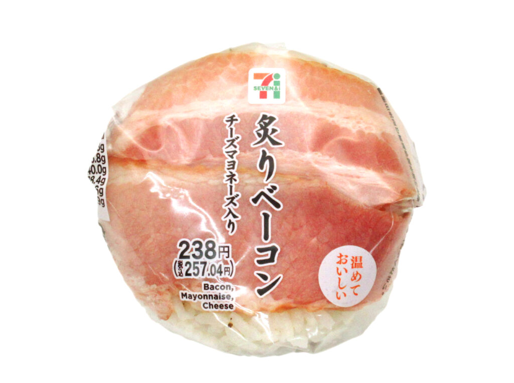 セブンイレブンの炙りベーコンおむすび（チーズマヨネーズ入）を比較する。税込価格：257円、カロリー：236kcal、たんぱく質：6.8g、脂質：5.8g、炭水化物：40g、糖質：38.4g、食物繊維：1.6g、食塩相当量：1.9g。表面に盛り付けたベーコンと中具を入れたチーズマヨネーズソースに相性のよい、ペッパーライスを合わせたおむすびです。アレルギー：卵、乳、小麦。