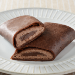 ローソンのくちどけショコラクレープを比較する。税込価格：265円、カロリー：270kcal、1円あたりカロリー：1.02kcal/円、たんぱく質：4.6g、1円あたりたんぱく質：0.02g/円、脂質：17.6g、炭水化物：24.3g、糖質：22.3g、食物繊維：2g、食塩相当量：0.2g。ココア風味の生地で、チョコソースとチョコホイップを包んだクレープ。アレルギー：小麦、卵、乳成分、大豆。