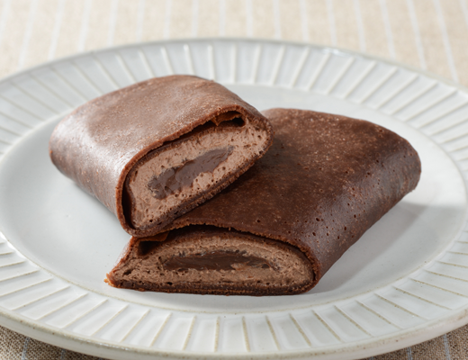 ローソンのくちどけショコラクレープを比較する。税込価格：265円、カロリー：270kcal、1円あたりカロリー：1.02kcal/円、たんぱく質：4.6g、1円あたりたんぱく質：0.02g/円、脂質：17.6g、炭水化物：24.3g、糖質：22.3g、食物繊維：2g、食塩相当量：0.2g。ココア風味の生地で、チョコソースとチョコホイップを包んだクレープ。アレルギー：小麦、卵、乳成分、大豆。
